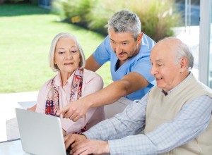 Male caretaker assisting senior couple in using laptop at nursing home porch
